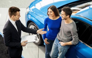 Top angle view of a salesperson selling a new car to a young couple | Featured image for First Time Car Buyer Tips blog by FinanceBeagle